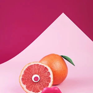 Surreal pink grapefruit with eye and lips on pink background
