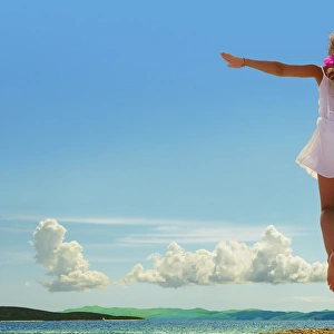 Woman jumping on beach, arms outstretched, rear view