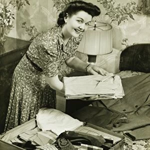 Woman putting clothes into suitcase, (B&W)