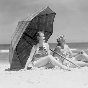 Two women sitting on beach under parasol