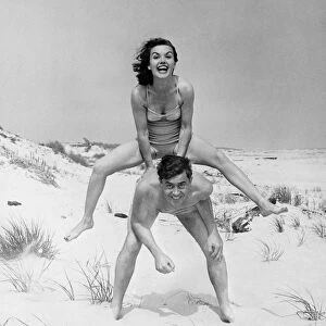 Young couple on beach, woman leap-frogging man, (B&W), portrait