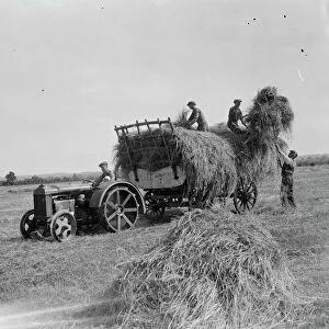 Farm workers in Farningham load hay on to the trailer being pulled by a tractor. 1935