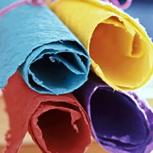 Four pieces of brightly coloured handmade paper rolled up and tied with pink string