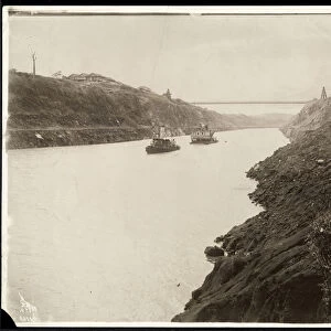 View of two boats in the Panama Canal during its construction with a suspension bridge