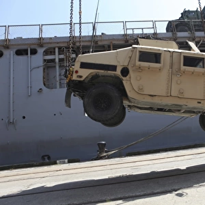 A crane lifts an M998 Humvee on the flight deck of USS Carter Hall