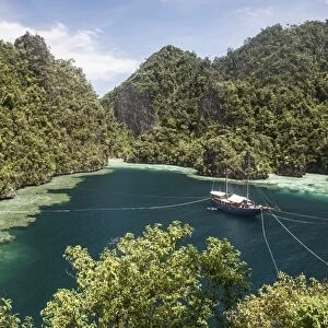 Rugged limestone islands frame an Indonesian pinisi schooner