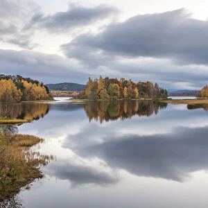 Autumn colours and stormy clouds reflected in the calm waters of Loch Insh, Cairngorms
