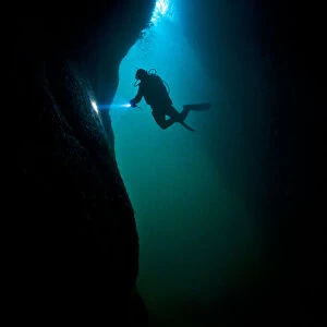 Scuba diver exploring a sea cave beneath Giants Legs, Bressay, Shetland Islands, Scotland