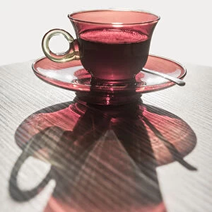 A Red Glass Cup A Saucer With A Beverage Reflected On A White Surface; Locarno, Ticino, Switzerland