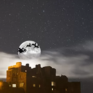 Santa In His Sleigh And Reindeer Silhouetted In The Starry Sky In Front Of The Moon Over Buildings; Bamburgh, Northumberland, England