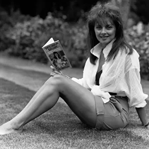 Carol Vorderman TV Presenter sitting on grass lawn holding paperback book