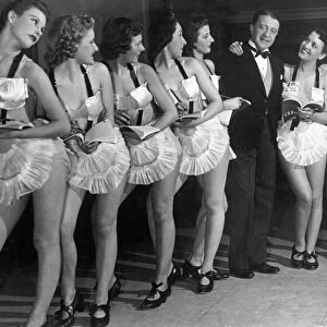Comedian Tommy Handley stands with a line up of modern girl secretaries at Jack