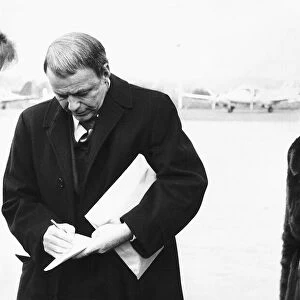 Frank Sinatra Actor and Singer writing on a piece of paper while standing at an airport