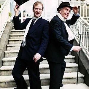 George Cole actor and Dennis Waterman standing on doorsteps raising a top hat and cane