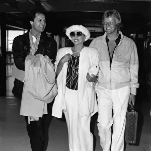 Joan Collins walking through Heathrow Airport with her boyfriend Peter Holm on her left