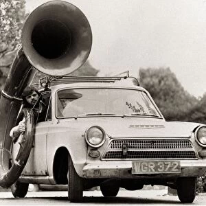 A man driving car with a large Sousaphone attached to the side Musical instruments