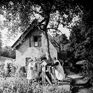 Mother and daughter winding up the bucket from the well in their cottage garden