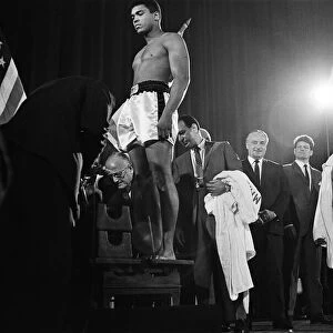 Muhammad Ali stands on the scales as Brian London looks on at the weigh-in ahead of their