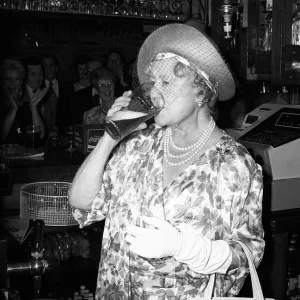 Queen Mother stands behind a pub bar drinking beer in July 1987