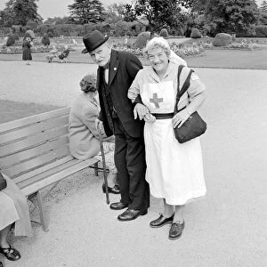 A Red Cross nurse helps and elderly gentleman to a bench during a day trip to Trentham