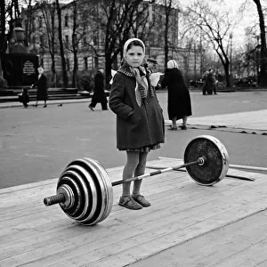Russian girl contemplates the dumb bell weights used by the weightlifters in a Moscow