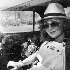 Singer Lulu in the back of a car wearing a trilby hat, sunglasses and dungarees
