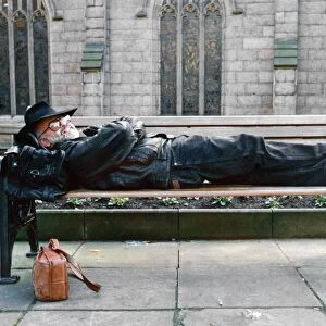 Terry Pratchett lying down on a bench. Pratchett is an English author of fantasy novels