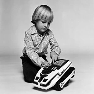 A young boy playing with a Big Trak toy, a programmable electric vehicle created by