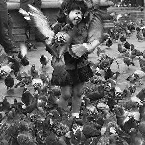 Young girl surrounded by hungry pigeons as she feeds them in Trafalgar Square