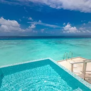 Infinity swimming pool with sea and ocean view on blue sky background. Luxury infinity pool over amazing turquoise lagoon and ladder into the water