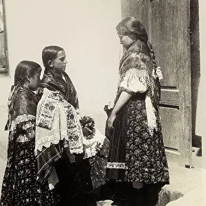 Three children, in Hungarian traditional dresses, standing up on the steps of a house of which a door can be glimpsed