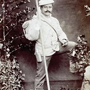 Full-length portrait of a young man dressed for an outing, with a stick in his hand. He is shown against a backdrop with bushes