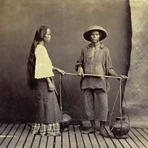 Full-length portrait of a young milk vender in Manila. He is wearing traditional humble dress and holding a pole from which two amphoras are hanging. Next to the man is a young woman with long hair seen in profile