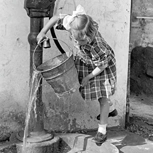 Little girl emptying a bucket of water in a pump fountain