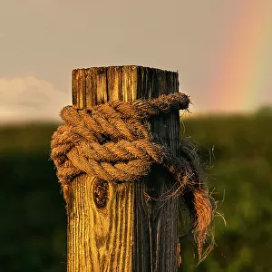 Wooden beam with rope tied around it, rainbow in background