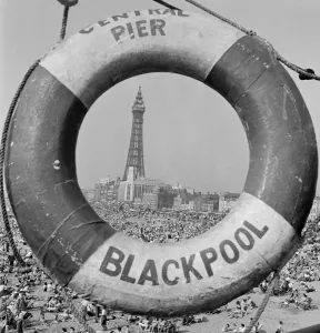 Prints of BLACKPOOL, Lancashire. General view along beach towards the Blackpool Tower seen through centre of ring of life buoy on central pier. Mid 20th century. John Gay Iconic Photographers of England - Historic Image Collections: Blackpool Print: Central Pier Beach Scene