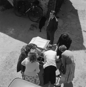 Prints of Thaxted, Essex. Looking down at a group of women cooing at a baby in a pram as a man looks on. Photographed by John Gay in the late 1950s Then and Now England - Historic Change Over Time: A late 1950s print of a scene in Thaxted, Essex