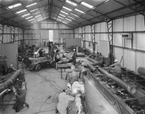 Prints of Bottesford Airfield, Bottesford, Melton, Leicestershire. The interior of a large corrugated steel fabrication shop at the Bottesford pre-yield depot, showing workers cutting and welding pipework Engineering And Construction Prints: Bottesford Airfield Print: Steel Fabrication Shop Interior
