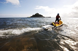 RNLI lifeguard on a rescue watercraft (RWC) with St Michaels Mount near Penzance in RNLI lifeguard on a rescue watercraft (RWC) with St Michaels Mount near Penzance in