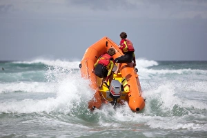 Two RNLI lifeguards heading through a breaking wave on an arancia inshore rescue boat, bow high out of the water Two RNLI lifeguards heading through a breaking wave on an arancia inshore rescue boat, bow high out of the water