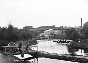 Prints of Blackwater at Benburb - a view along the river to a weir with buildings behind and a man and lady on a wooden bridge to the left, in the foreground Tyrone Prints: Blackwater at Benburb Print - Early 1900s Northern Ireland
