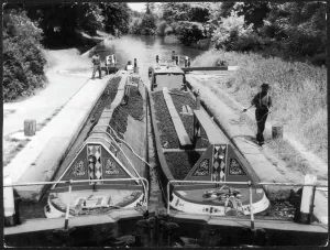 Prints of A pair of laden narrow boats, with their cargoes of coal, passing through a lock on the Grand Union Canal near Watford, Hertfordshire, England Hertfordshire Prints: Coal Narrow Boats Print - Grand Union Canal Lock Scene