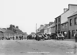 Prints of The Diamond, Carndonagh - a street scene with a market going on at the side of the road. There are people and hand carts. (Location: Republic of Ireland: County Donegal: Carndonagh) Republic Of Ireland Prints: Early 20th Century Print of Carndonagh Market Scene