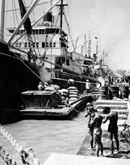 Prints of Unloading a shipment of cargo from ships in Manila docks, Philippines. Three young men in shorts wipe the sweat from themselves in the heat. Date: late 1930s Related Prints: Manila Docks Print, Late 1930s