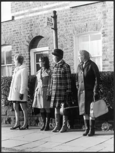 Prints of A young pregnant woman waiting at a bus stop with another young woman and two old ladies Transport Prints: Bus Stop Queue Print 1960s