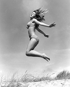Young woman leaps up from a sand dune, Cornwall Young woman leaps up from a sand dune, Cornwall