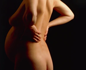 Naked pregnant woman at full-term holds her back Naked pregnant woman at full-term holds her back