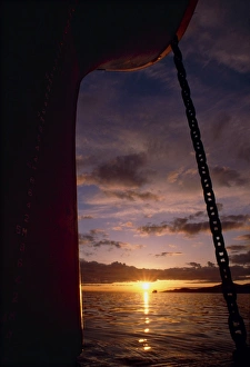 Setting sun framed by bow & anchor line of ship Setting sun framed by bow & anchor line of ship