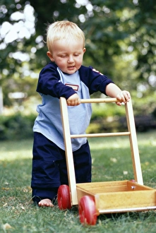 Prints of MODEL RELEASED. First steps. One-year-old boy holding onto a trolley as he takes his first steps Images Dated 2004 April: First Steps Print: One-year-old boy takes his first steps holding a trolley