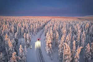 Finland Collection: Aerial view of car on icy road and illuminated headlamps driving in the snowcapped forest